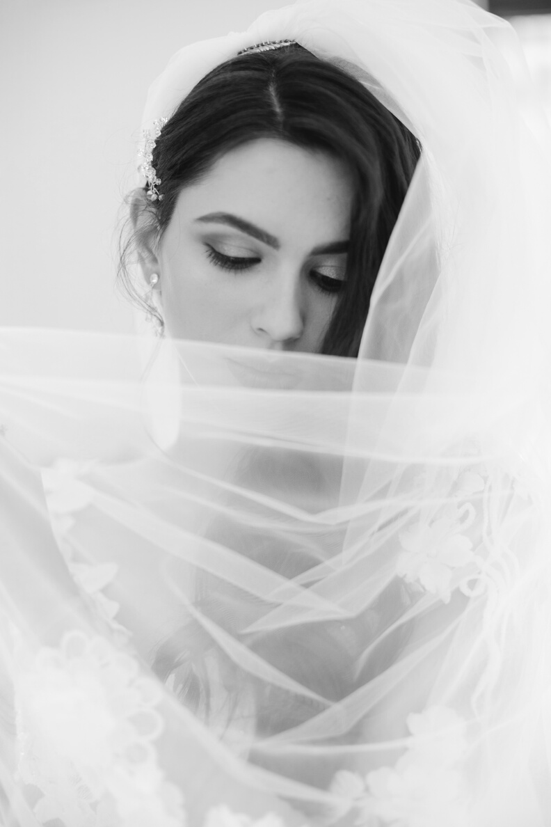 Beautiful young bride covering face with veil while posing